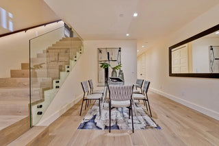 Dining room with glass table, six chairs, modern art, and glass-railed staircase. Los Gatos, CA home staging example.