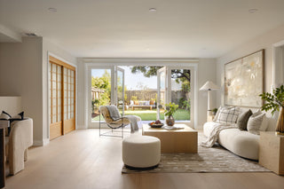 Modern living room with white furniture, large windows, and a view of a garden.