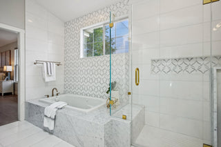 A_Marble_tub_glass_shower_patterned_tile_wall_and_window._White_towels_hang_by_the_tub