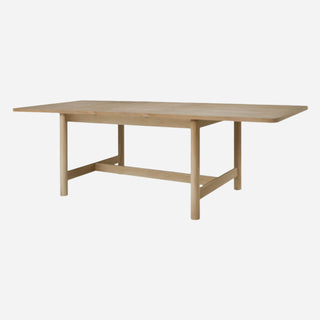 A beige Bloomfield dining table with a butterfly extension, made of wood, with rounded corners and tubular legs.