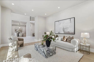 A bright living room featuring white furniture and a colorful painting on the wall, creating a modern and inviting atmosphere.