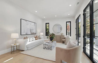 A bright living room featuring white furniture and large windows that allow natural light to fill the space.