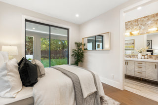 Modern bedroom with a bed, window, and bathroom in the background.