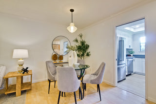 Modern dining area with round glass table and gray chairs, adjacent to a kitchen.