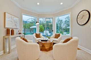 Living room with beige armchairs, a coffee table, and large windows.