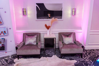 Two gray armchairs with pink cushions in a room with pink lighting and a TV on the wall.