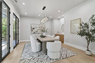 A dining room featuring white walls and a large window, allowing natural light to fill the space.