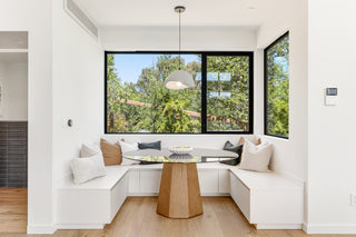 A  entryway with a wooden door, textured gray console, white vase with branches, abstract wall art, and large window showing an outdoor environtment   modern patio .