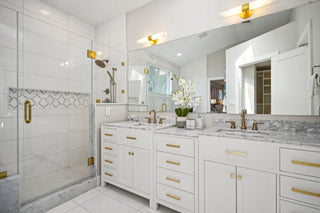 A_mirror_dual_sinks_on_a_marble_countertop_white_cabinetry