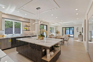A modern dining table with kitchen light walls and wooden flooring, abstract art on the wall, gray couch, and large windows