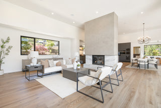 A modern entryway with a wooden door, textured gray console, white vase with branches, abstract wall art, and large window showing an outdoor patio.