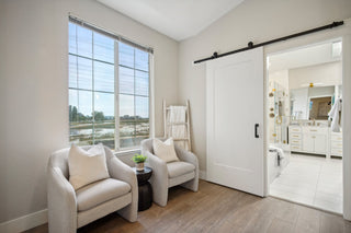 A_room_with_two_cozy_armchairs_pillows_and_a_small_table_with_a_plant_by_a_bathroom.