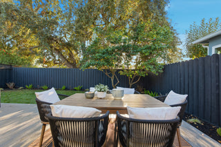 Outdoor dining area with wooden table and chairs in a backyard setting.