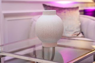 White textured vase on a glass table with a blurred indoor background