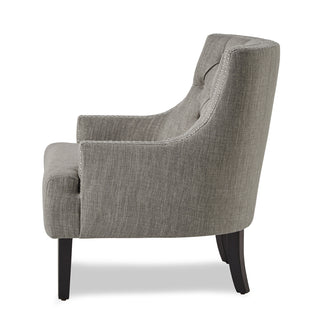 A textured taupe fabric upholstered accent chair with high-polish nailhead trim, a button-tufted back, and black wood legs left site.