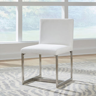 An upholstered dining chair with pearl white fabric and brushed stainless steel legs, positioned in a room with natural lighting.