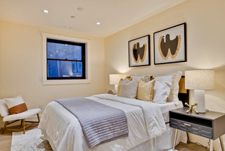 Neatly made bed in a bedroom with two lamps and wall art.