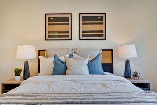 Bedroom with a neatly made bed, two lamps, and framed artwork on the wall.