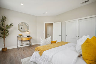 Bedroom_featuring_a_white_bed_mustard_yellow_accents_a_wooden_desk_with_an_octagonal_mirror_and_light_gray_walls