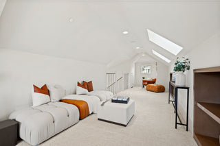 Modern living room with a white sectional sofa, orange cushions, and a staircase in the background.