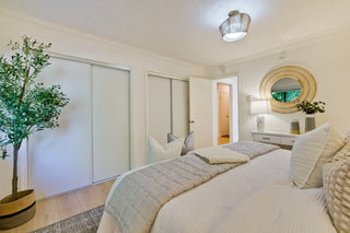 Neatly made bed in a bedroom with a plant and mirror.