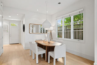 Modern dining area with wooden table and white chairs near a window with a view of greenery.