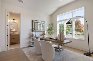Bright home office with a large window, modern wooden desk, two white chairs, and a floor lamp. A mirror and plants add a serene touch. Neutral tones.