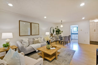 Bright_living_room_with_beige_sofas_wooden_coffee_table_and_abstract_wall_art._Open_dining_area_features_a_round_table_gray_chairs_and_pendant_light