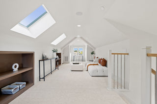 Attic bedroom with skylights, bookshelves, and a view of a living room.