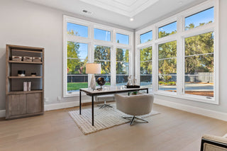 Modern living room with white sofas, decorative pillows, and a round coffee table with a plant. Large glass doors open to a green view, creating a serene atmosphere.