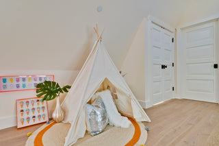Children's playroom with a white teepee, decorative pillows, and a plant.