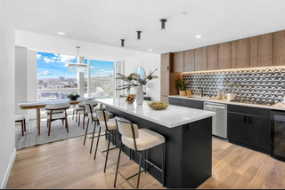 Modern kitchen with a large island, wooden cabinets, and a cityscape view.