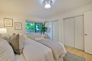 Cozy_bedroom_with_neutral_tones_featuring_a_neatly_made_bed_soft_pillows_a_window_with_greenery_outside_framed_art_and_a_modern_light_fixture