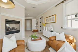 Cozy living room with caramel leather chairs, white cushions, and a modern fireplace. A round ottoman and potted plants add warmth and elegance.