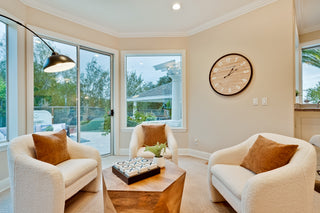 Living room with beige armchairs, a coffee table, and a clock on the wall.