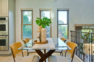 Dining room with a glass table and yellow chairs, large windows, and a view of greenery outside.