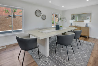 Modern dining room with a long table and chairs on a patterned rug.