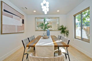 Dining room with a long wooden table and chairs, abstract art on the wall, and a large window.