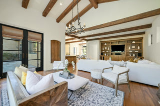 Dining room with wooden floors, a round glass table, and four black chairs. Modern art, a chandelier, and large windows create an invitings atmosphere.