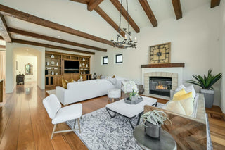 Dining room with wooden floors, a round glass table, and four black chairs. Modern art, a chandelier, and large windows create and invitings atmosphere.