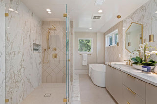 Elegant bathroom with glass shower featuring marble tiles, a freestanding bathtub by a window, modern vanity with twin sinks, and gold accents for a luxurious feel.