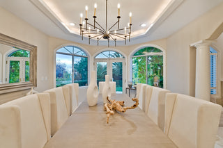 Modern dining room with a chandelier, large windows, and a decorative piece on the table.