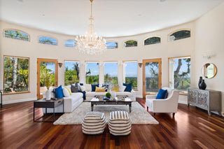 Elegant living room with an beige sofas, armchair, and wooden coffee table. Large windows offer a scenic view of trees and hills, creating a serene ambiance.