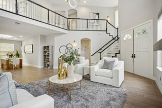Elegant_room_with_modern_decor_featuring_white_sofas_a_fluffy_gray_rug_and_a_round_marble_coffee_table_adorned_with_gold_vases_and_greenery._A_large_staircase_with_dark_railing