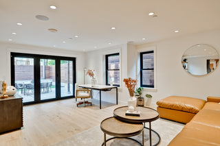 Modern living room with a brown leather sofa, round coffee table, and large mirror on the wall.