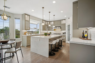 Kitchen_featuring_taupe_cabinetry_a_large_white_waterfall_island_with_bar_stools_wood_flooring_and_ample_natural_light_from_bay_windows.