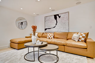 Modern living room with a brown leather sectional sofa, round coffee tables, and decorative elements.