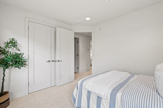 Bedroom with white walls, a bed with striped bedding, and a plant.