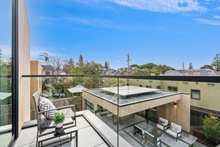 Modern balcony with glass railings, outdoor furniture, and a clear blue sky.