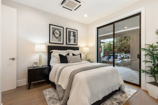 Modern bedroom with a bed, nightstands, and a view of the outdoors through glass doors.